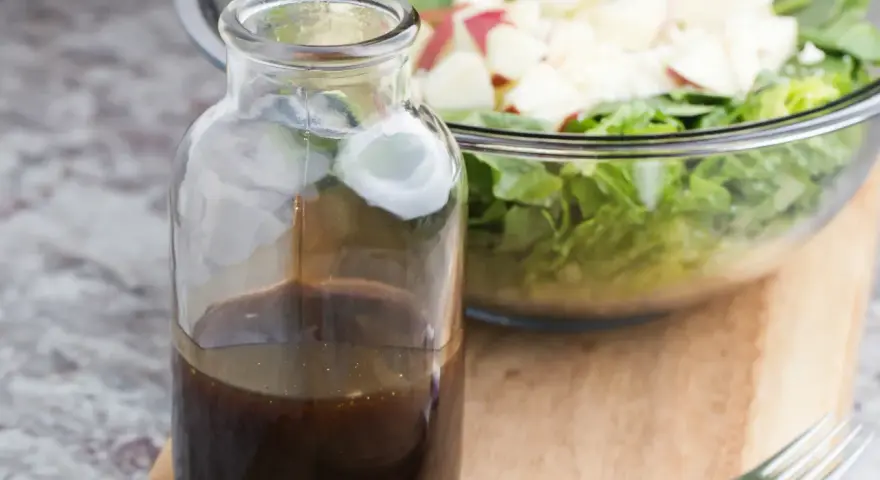 Bouteille de sauce salade facile, prête à être versée sur une salade fraîche et croquante dans un bol en verre.