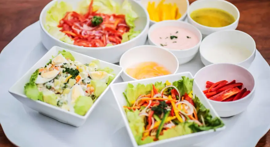 Assortiment de salades colorées avec plusieurs options de sauce pour salade, dont une rose et une verte.