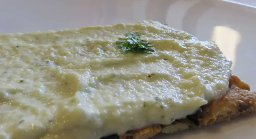 Houmous de courgette crémeux sur une tranche de pain complet, garni d'une touche de persil frais.