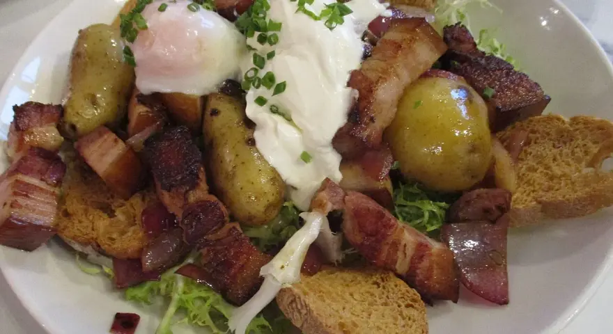Une généreuse salade vosgienne avec des pommes de terre, lardons, œuf poché et croûtons sur un lit de verdure.