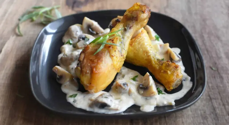 Deux pilons de poulet dorés baignent dans une sauce crémeuse aux champignons, garnie d'herbes fraîches. Un délice de poulet à la crème.