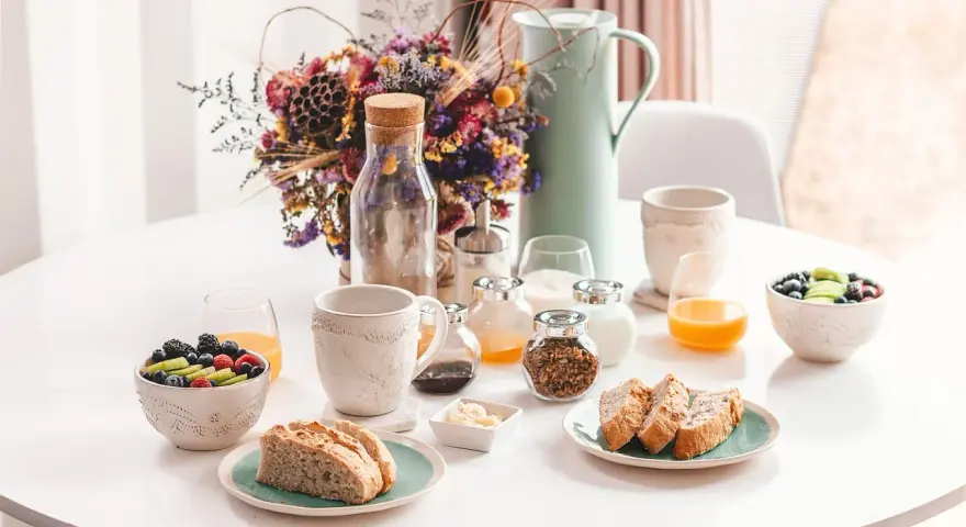 Un délicieux déjeuner vegan avec fruits frais, pain artisanal, granola et jus d'orange, présenté sur une table blanche.