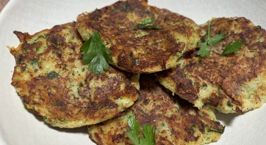 Galettes dorées de courgette et pomme de terre, garnies de persil frais, prêtes à être dégustées.