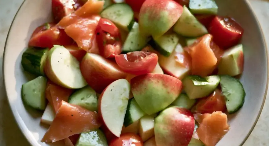 Salade fraîche et colorée : morceaux de concombre, tomates cerises, pommes rouges et saumon fumé, le tout servi dans un bol.