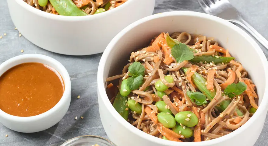 Pâtes soba aux edamames, carottes râpées et coriandre, servies avec une sauce crémeuse. Un délice sain et coloré.