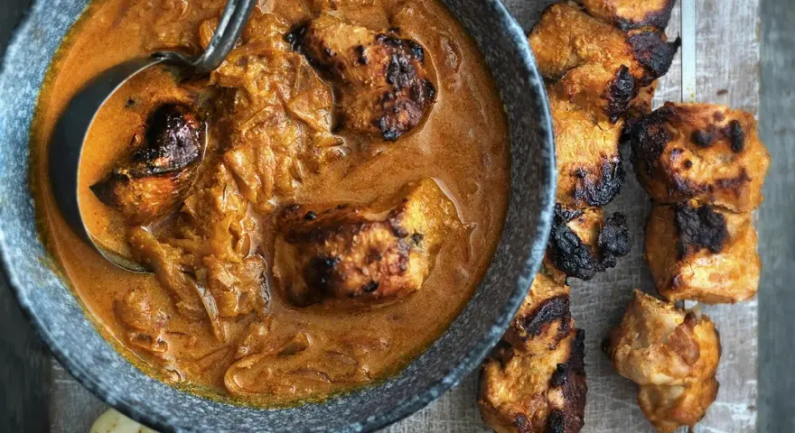 Un plat de poulet tikka savoureux, avec des morceaux de poulet grillés dans une sauce crémeuse et des accompagnements comme du pain naan et des quartiers de citron.