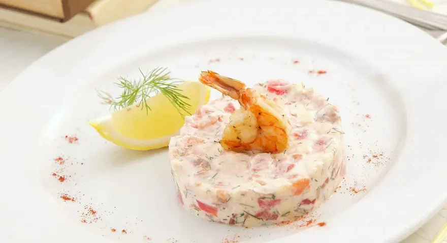 Délicieux tartare de crevette thaï, garni d'une crevette grillée et d'une tranche de citron, sur une assiette blanche.