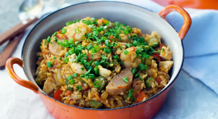 Un plat de jambalaya coloré, garni de crevettes, poulet, saucisse et oignons verts. Une recette savoureuse à découvrir.