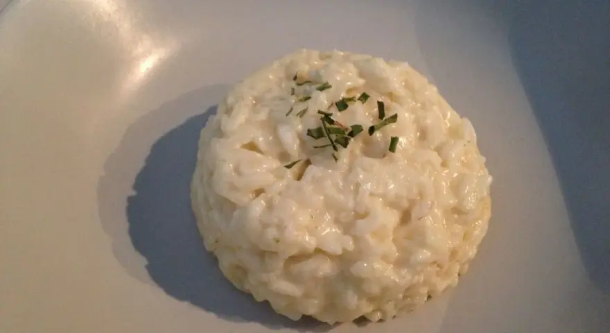 Un crémeux risotto coco, parsemé de ciboulette fraîche, repose sur une assiette claire.