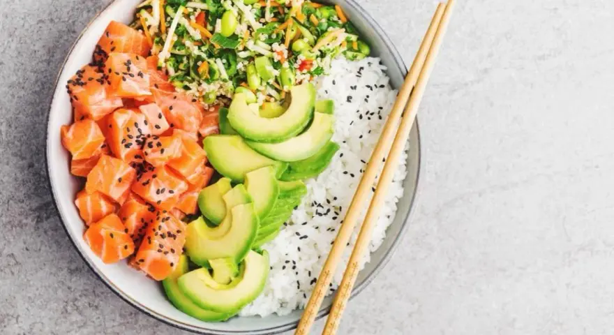 Un délicieux base poke bowl avec saumon cru, avocat, riz blanc et légumes croquants, prêt à être dégusté avec des baguettes.