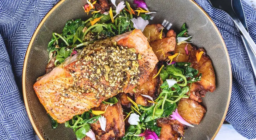 Un filet de saumon croustillant, garni de graines, servi avec des pommes de terre rôties et une salade verte. Un accompagnement poisson savoureux et coloré.