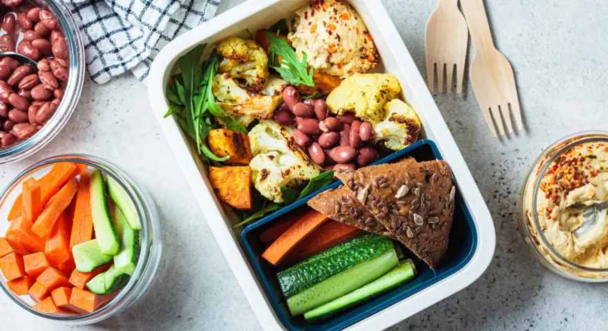 Un repas tiré du sac sain et coloré : houmous, légumes rôtis, haricots rouges, pain complet et crudités. Parfait pour un déjeuner sur le pouce.