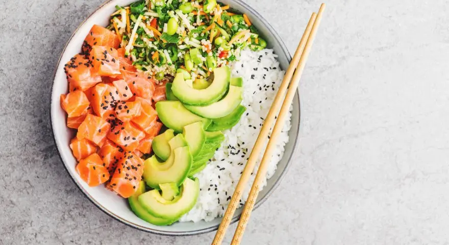 Un délicieux poke bowl santé avec saumon cru, avocat, riz blanc et légumes croquants, prêt à être dégusté avec des baguettes.