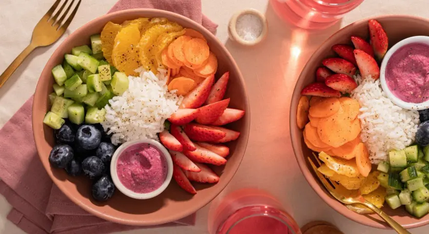 Deux bols colorés remplis de riz, fraises, myrtilles, concombre, carottes et oranges. Une belle idée poke bowl pour un repas frais et sain.