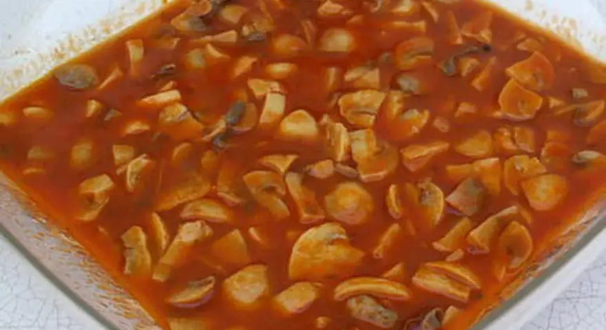 Champignons à la grecque, une préparation savoureuse de champignons coupés en morceaux, mijotant dans une sauce tomate riche et parfumée.