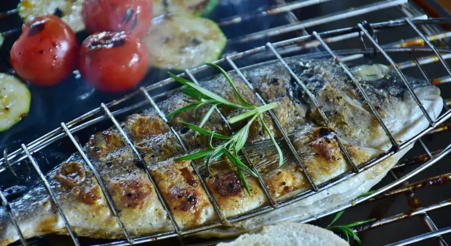 Dorade au barbecue, grillée à la perfection avec des tomates et courgettes, garnie de romarin. Un délice estival.