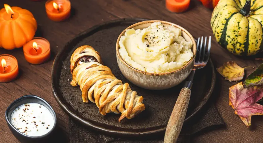 Un délicieux menu d'Halloween pour adultes : une momie feuilletée, purée de pommes de terre et sauce crémeuse, le tout dans une ambiance tamisée par des bougies.