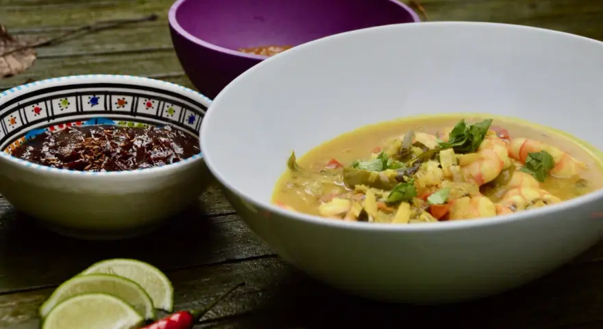 Un plat de crevette curry coco crémeux, garni de coriandre fraîche, servi avec des quartiers de citron vert et un piment rouge.