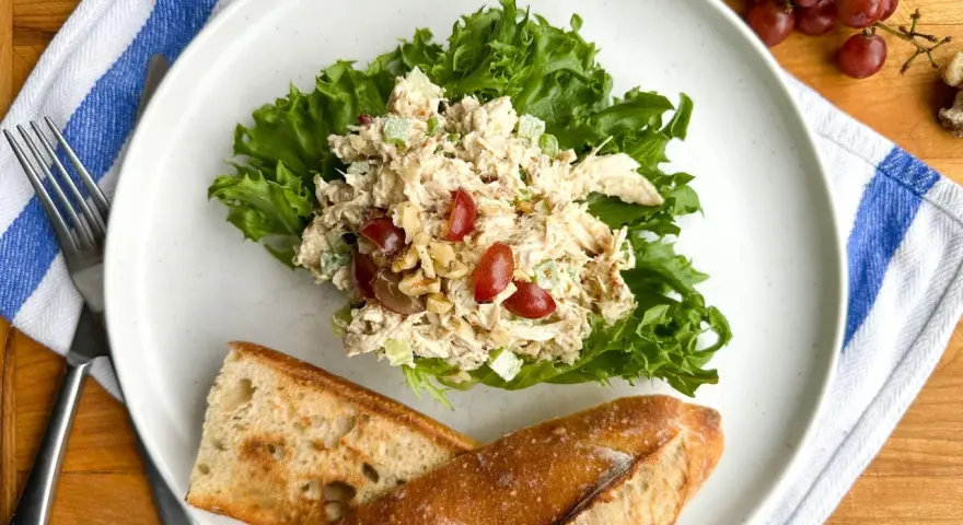 Salade de poulet froid mayonnaise sur laitue, avec des raisins et des noix, servie avec du pain croustillant.