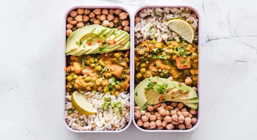 Deux lunch box remplies d'une idée lunch box école saine : curry de légumes, riz, pois chiches et avocat.