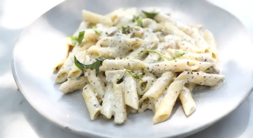 Pâtes penne nappées d'une sauce crémeuse à l'ail, parsemées de fines herbes fraîches, servies sur une assiette blanche.