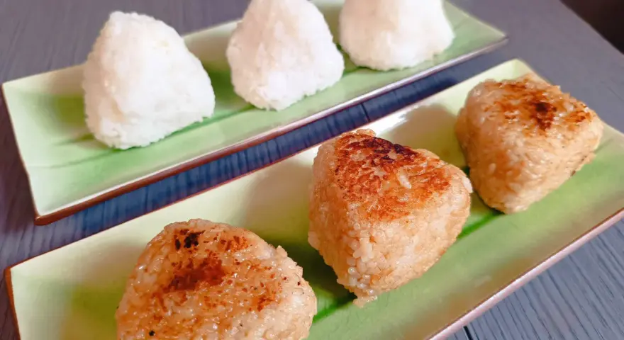 Sur des assiettes vertes, des onigiris nature et grillés, parfaits pour un pique-nique japonais.