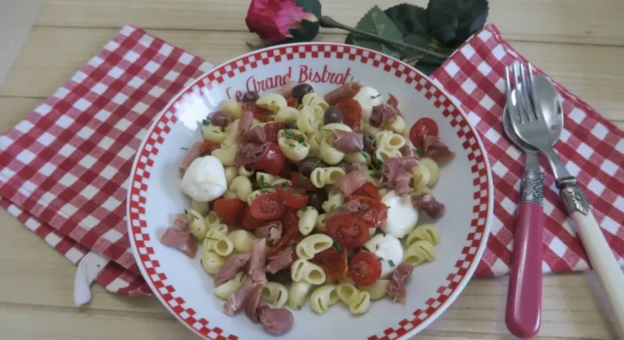 Une savoureuse salade italienne de pâtes avec tomates cerises, mozzarella, olives et jambon cru, garnie de ciboulette.