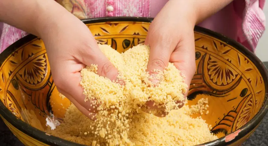 Mains travaillant du couscous marocain dans un plat traditionnel décoré.
