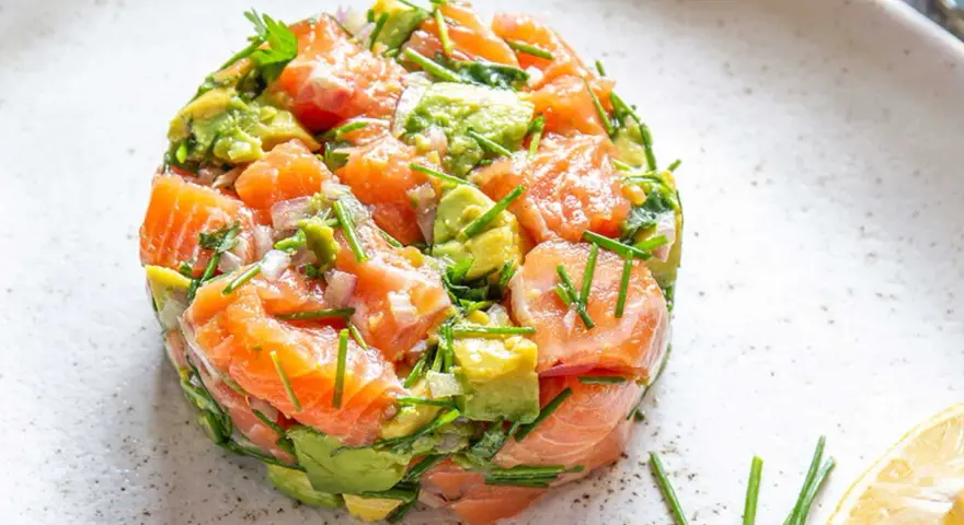 Un délicieux tartare saumon avocat, frais et coloré, garni de ciboulette et servi avec un quartier de citron.