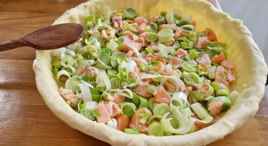 Préparation d'un plat végétarien : une tarte garnie de saumon et de poireaux coupés, prête à être cuite.