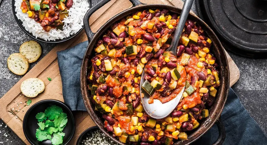 Un plat de chili végétarien copieux avec des haricots rouges, du maïs et des courgettes, servi avec du riz blanc.