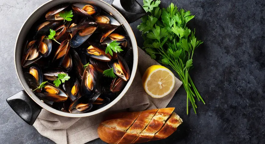 Un plat de moules au rosé, garni de persil frais, avec un quartier de citron et une baguette à l'ail.