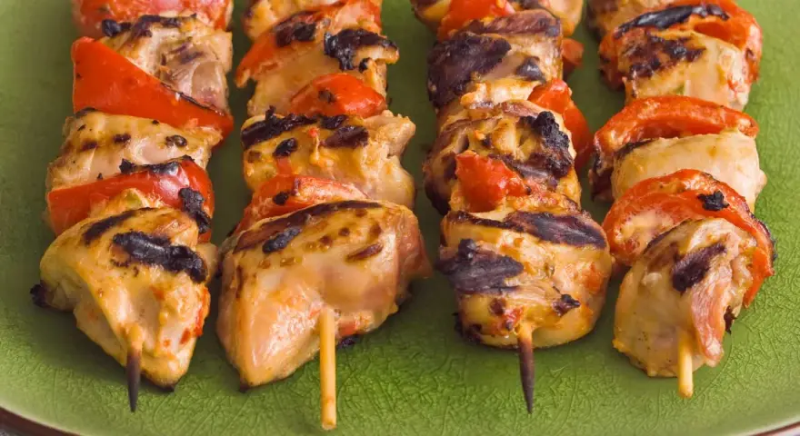 Brochettes de poulet grillé avec poivrons rouges sur une assiette verte. Parfait pour savoir quoi servir avec des brochettes de poulet.