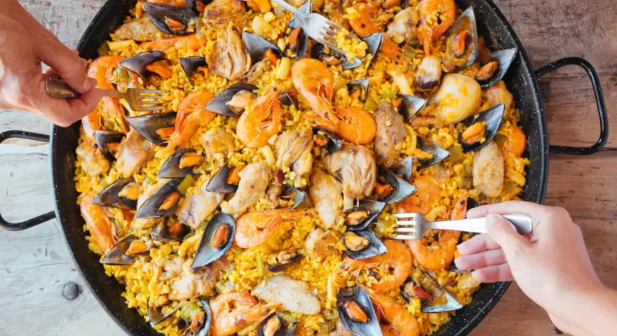 Un plat généreux de poulet paella, garni de crevettes et de moules, prêt à être dégusté par plusieurs mains.