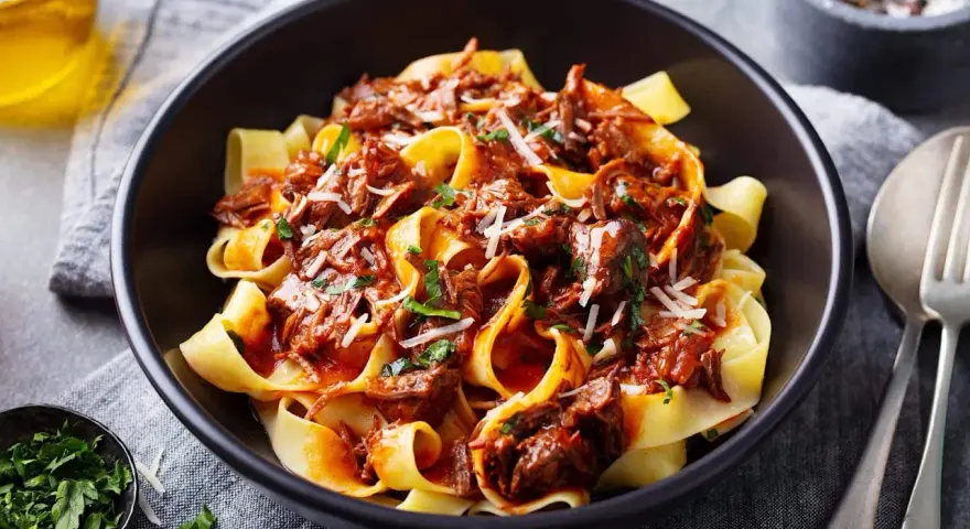 Pâtes larges nappées d'une riche sauce à la palette de boeuf effilochée, parsemées de parmesan et de persil frais.