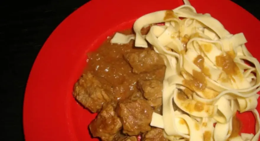 Un plat de pâtes fraîches avec un riche boeuf vindaloo, servi sur une assiette rouge vif.