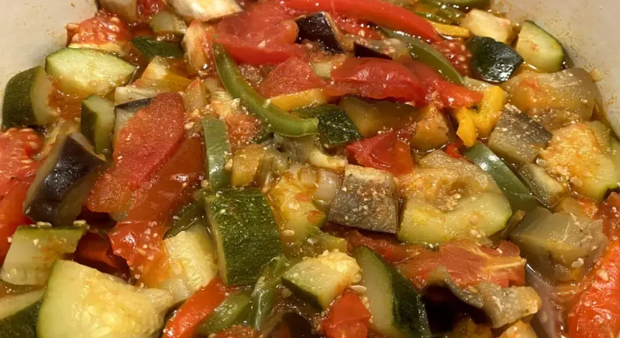 Un plat coloré de ratatouille niçoise, avec des morceaux de courgettes, aubergines, tomates et poivrons mijotés.