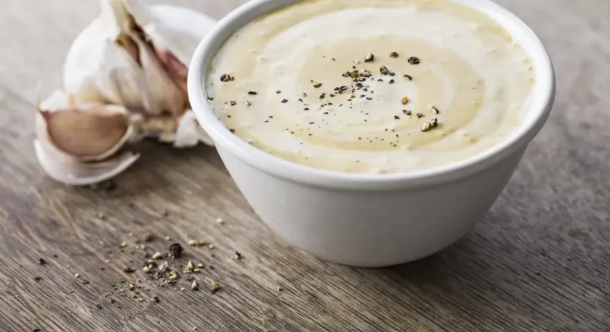 Sauce césar sans oeuf crémeuse, parsemée de poivre noir, avec une tête d'ail en arrière-plan sur fond de bois.