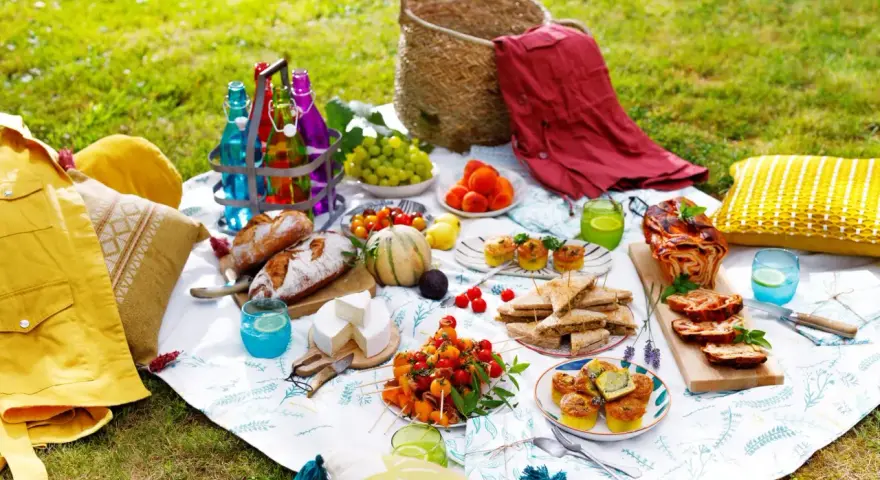 Un pique-nique gourmand sur l'herbe : pains, fromages, fruits, mini quiches, sandwichs, roulé salé, et boissons colorées. Une belle idée pique-nique !