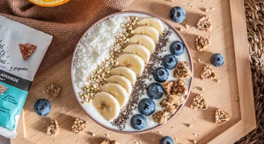 Un bol de smoothie aux fruits, bananes, myrtilles, noix de coco râpée et graines. Idéal pour manger sain le midi, avec des encas du supermarché.