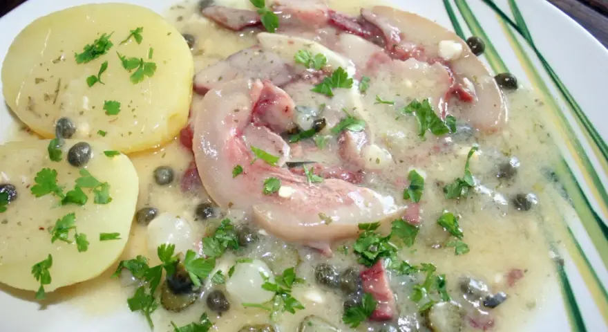 Tête de veau en sauce avec des pommes de terre et des câpres, garnie de persil frais.