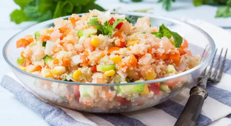 Salade quinoa colorée avec des dés de tomates, carottes, concombre et maïs, garnie de feuilles de menthe fraîche.