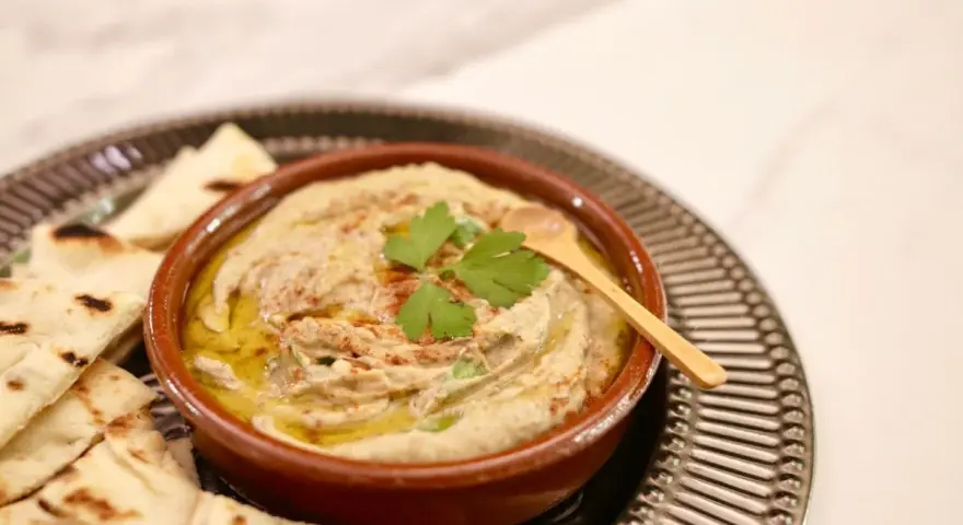 Un bol de baba ganoush crémeux, garni de persil frais et d'un filet d'huile d'olive, servi avec des pains pita grillés.