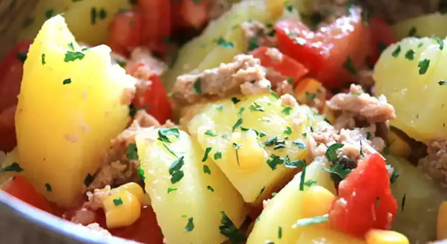 Salade de pommes de terre, thon, tomates et maïs, garnie de persil frais. Un plat simple et savoureux.