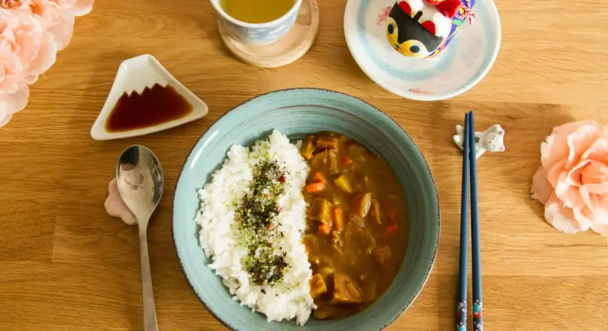 Un délicieux curry japonais avec du riz blanc, servi avec une tasse de thé et des décorations mignonnes.