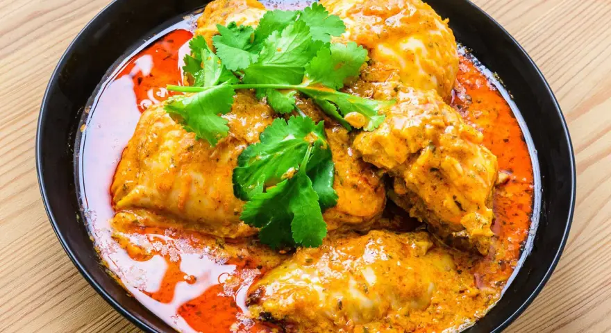 Un plat de poulet vindaloo, un curry indien épicé, servi dans un bol noir avec de la coriandre fraîche.