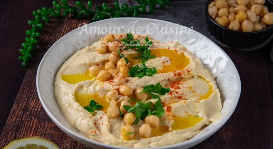 Un plat de houmous crémeux, garni de pois chiches, persil et paprika. Parfait pour découvrir 7 recettes de houmous maison.