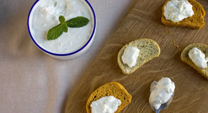 Un bol de crème tzatziki frais, garni de menthe, est servi avec des toasts.
