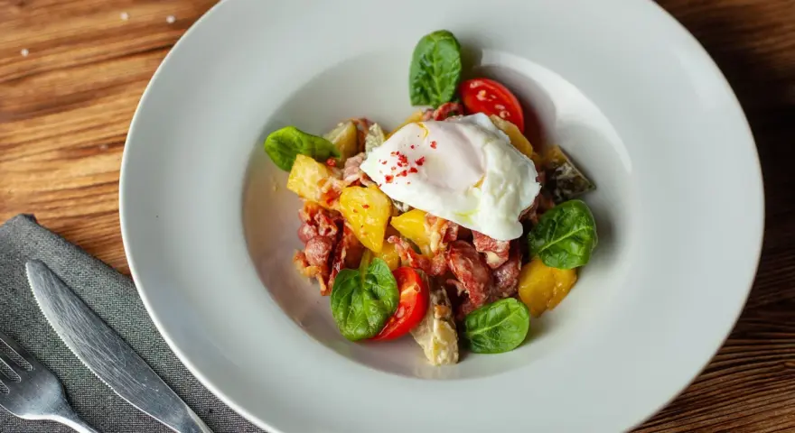 Salade colorée avec œuf poché, tomates cerises, lardons et quelques feuilles de salade légumes verts.