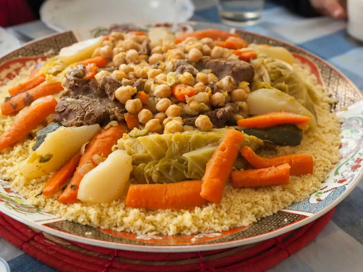 Un plat généreux de couscous algérien, garni de morceaux de viande, de carottes, de pois chiches et de chou.